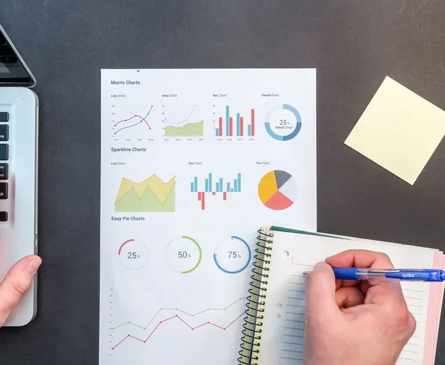 Charts and a notebook on a desk beside a laptop