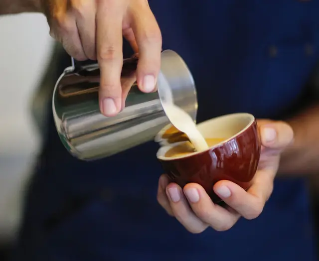 A barista pouring milk into a latte