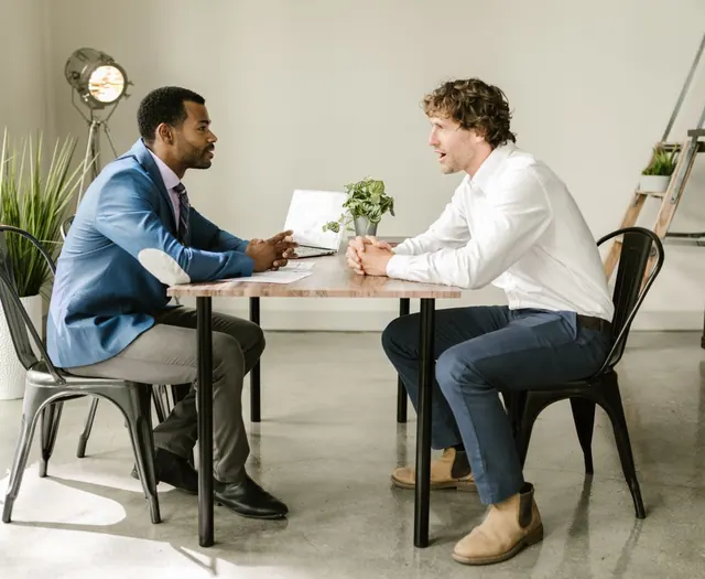 Two people talking across a table with a laptop